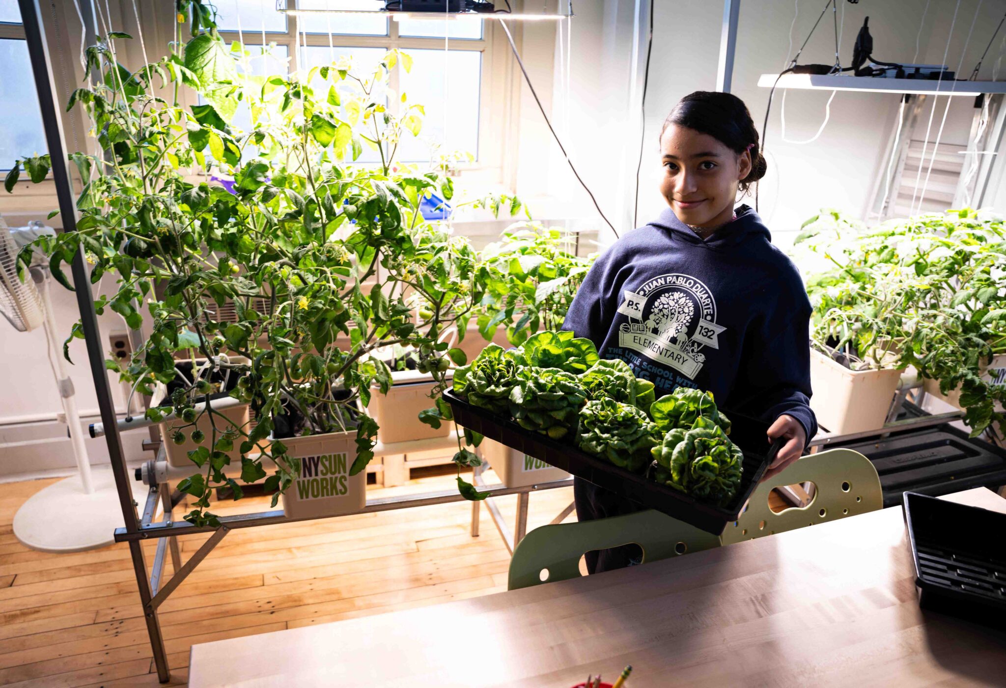 Student at PS132 holds a tray of harvest in front of VCS